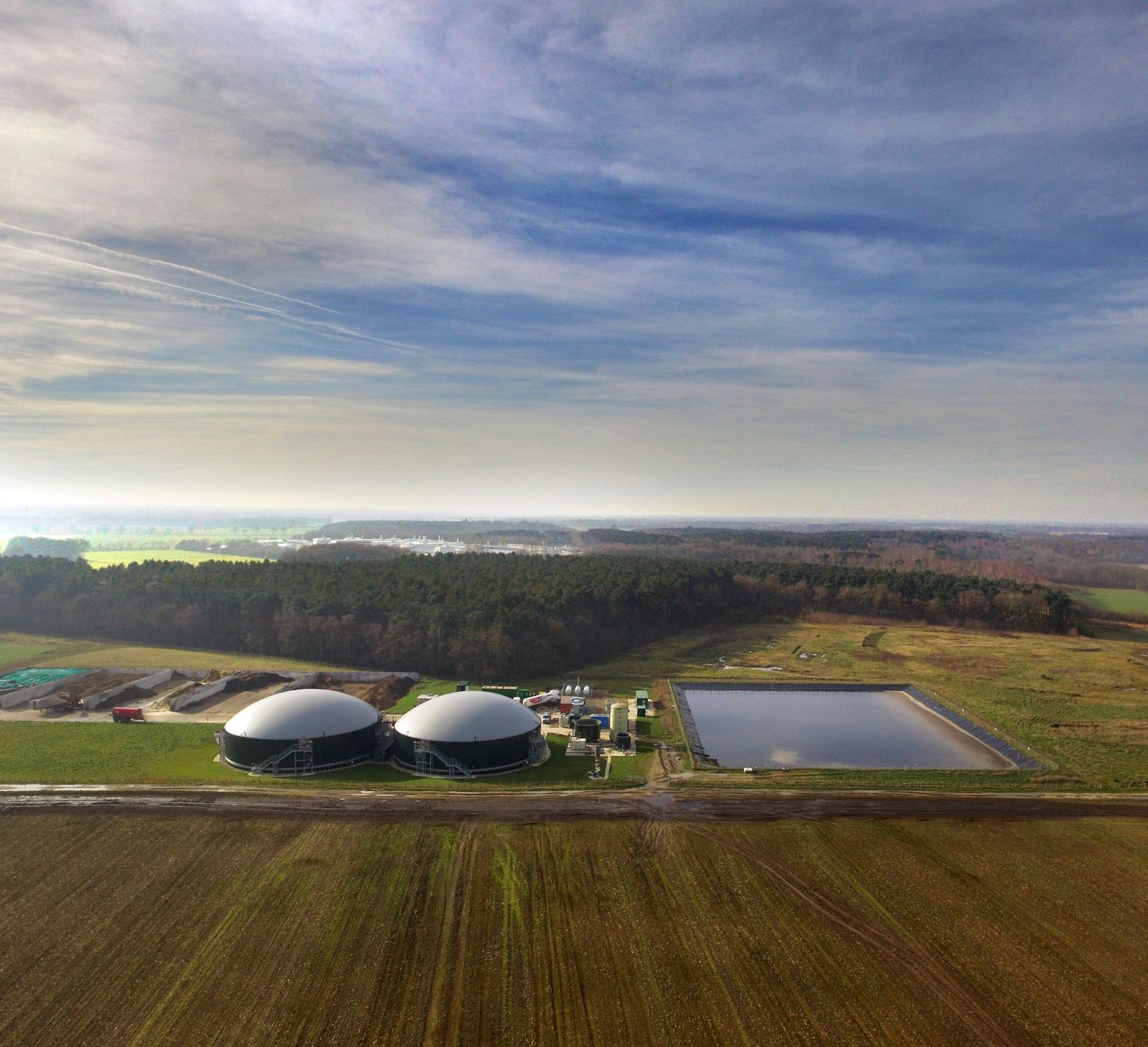 Aerial view of Gravel Pit Biogas: two digester domes and a lagoon among fields under a wide sky
